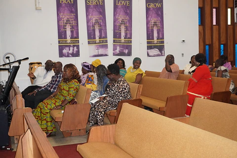 Members seated beside the Pray, Serve, Love, and Grow banners